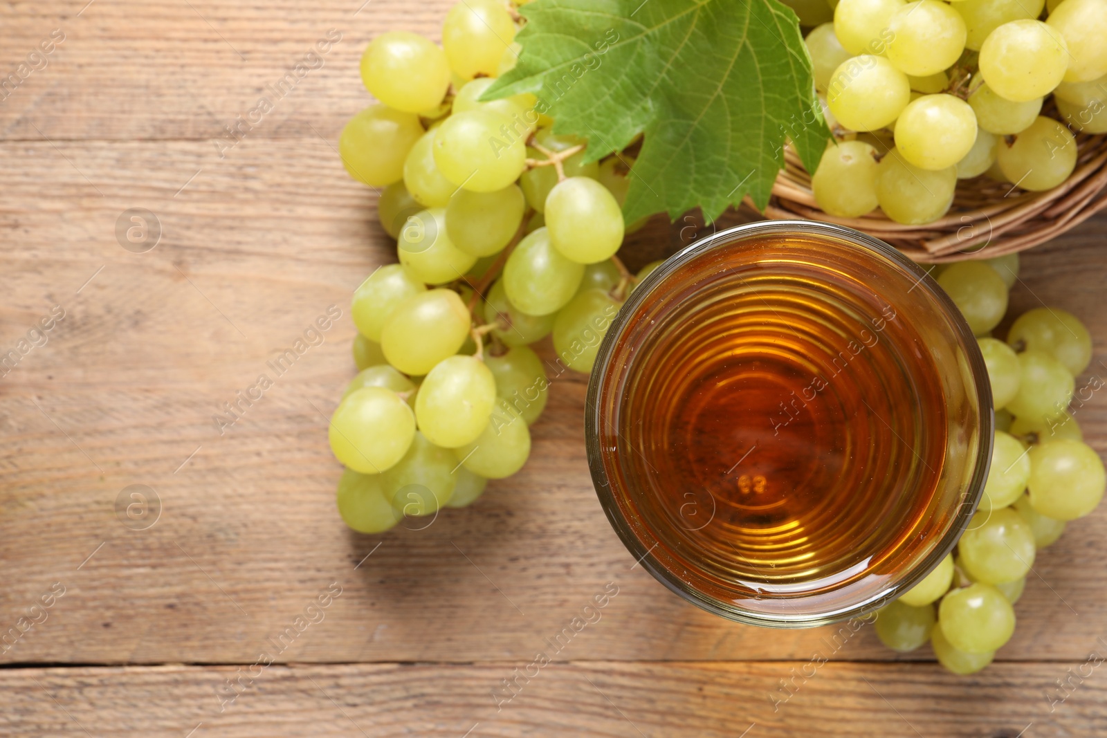 Photo of Tasty juice in glass, fresh grapes and leaf on wooden table, top view. Space for text