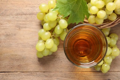 Tasty juice in glass, fresh grapes and leaf on wooden table, top view. Space for text