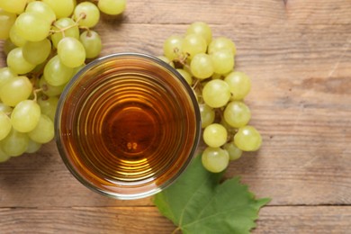 Photo of Tasty juice in glass, fresh grapes and leaf on wooden table, top view