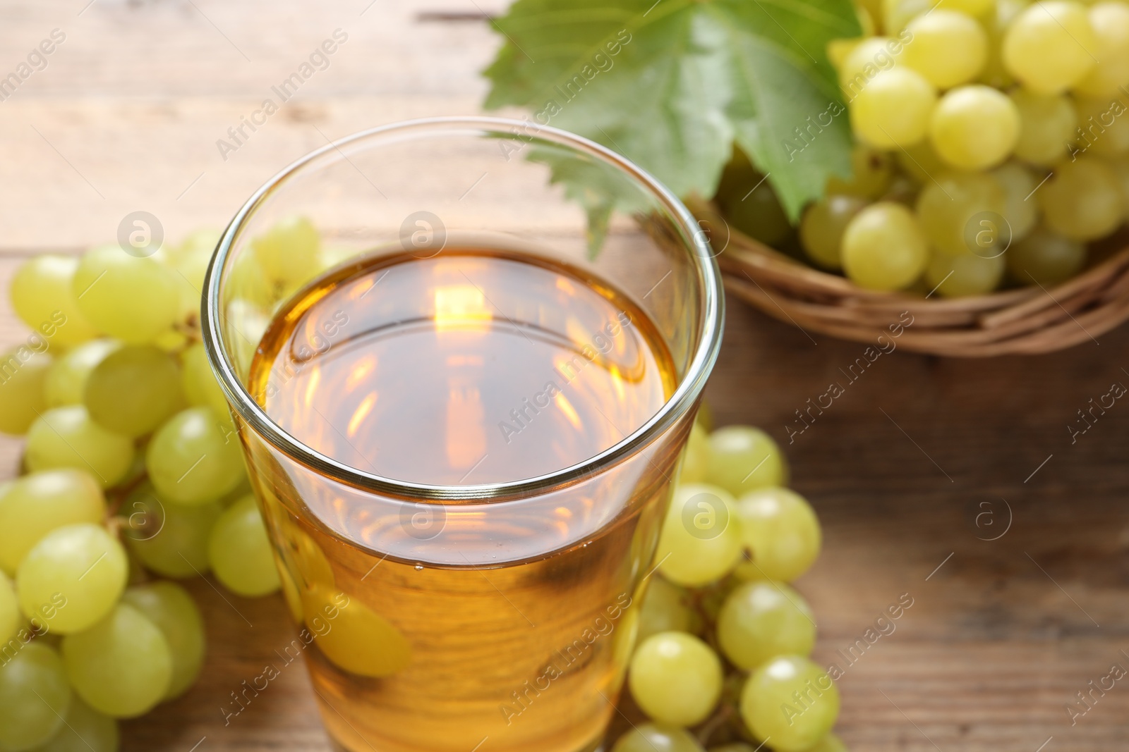 Photo of Tasty juice in glass, fresh grapes and leaf on wooden table, closeup