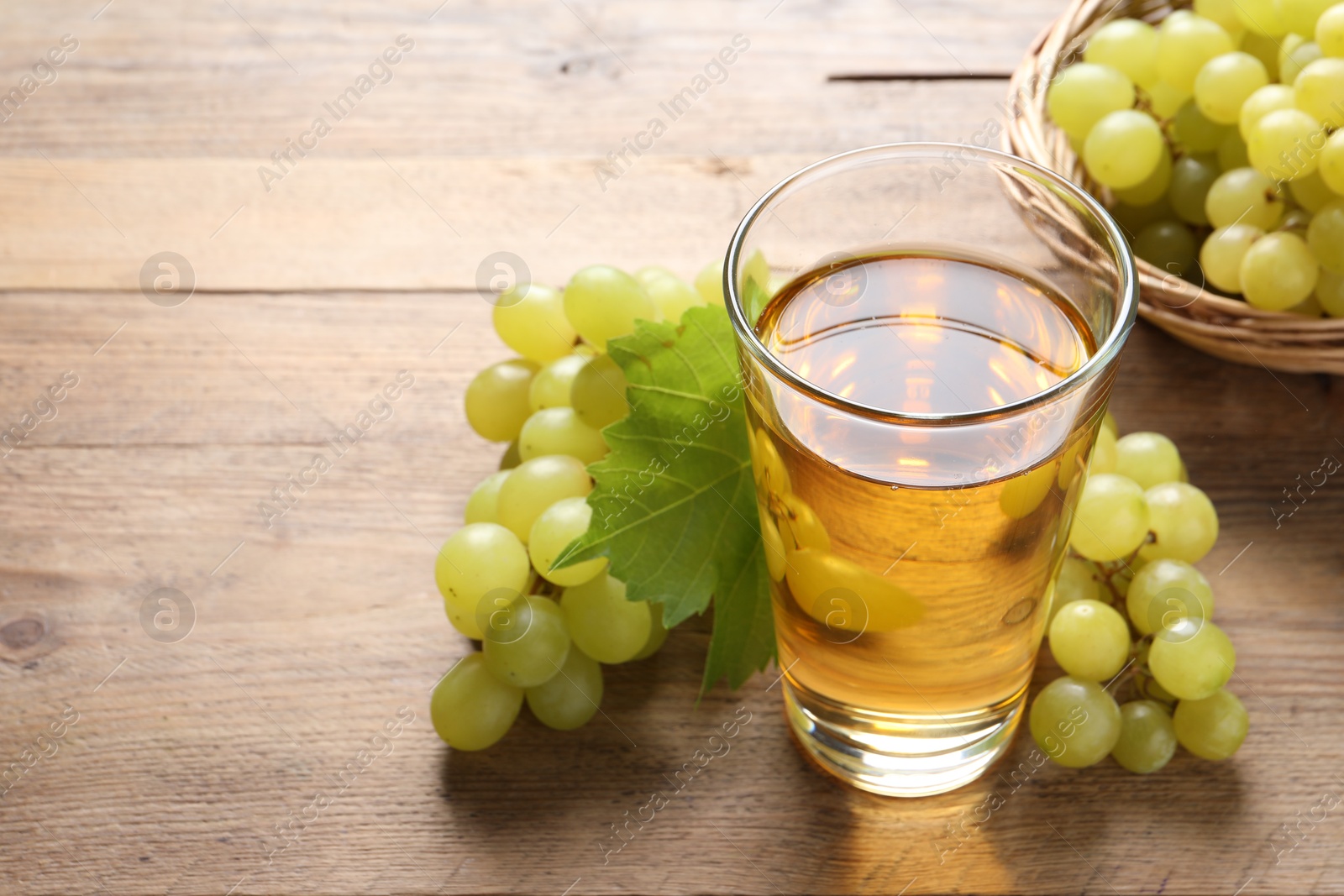 Photo of Tasty juice in glass, fresh grapes and leaf on wooden table, closeup. Space for text