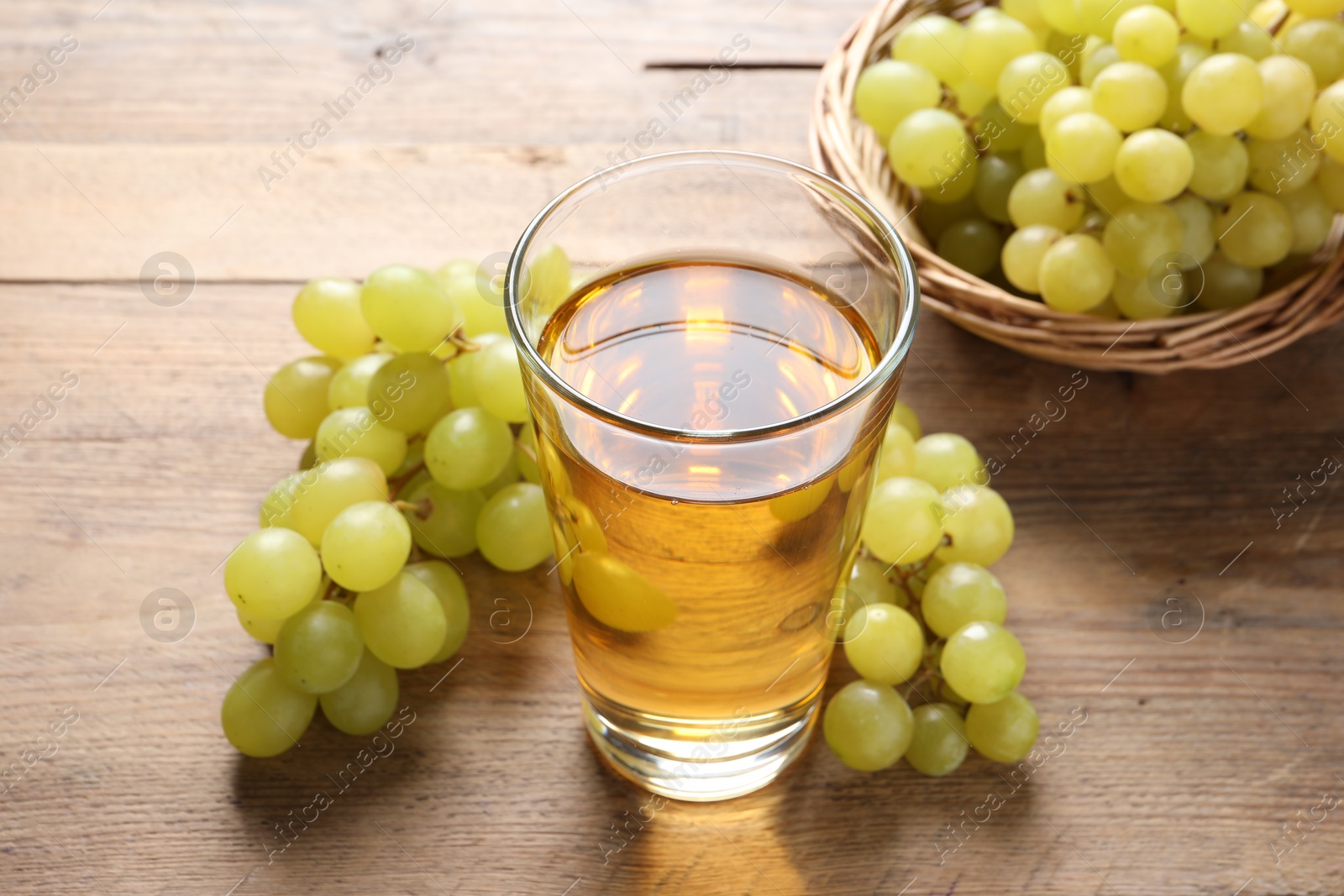 Photo of Tasty juice in glass and fresh grapes on wooden table, closeup