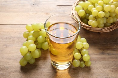 Photo of Tasty juice in glass and fresh grapes on wooden table, closeup