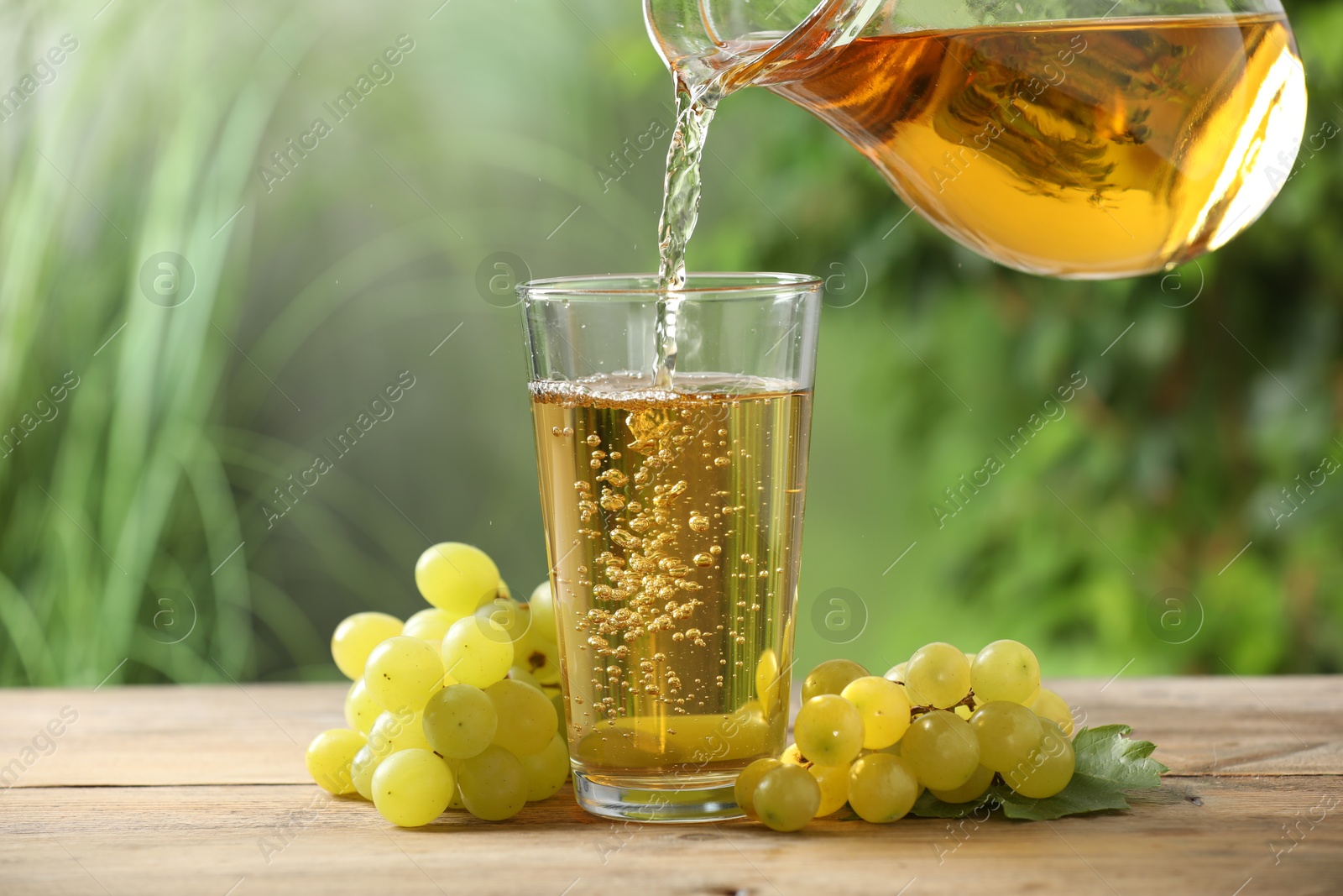 Photo of Pouring tasty grape juice into glass at wooden table outdoors, closeup