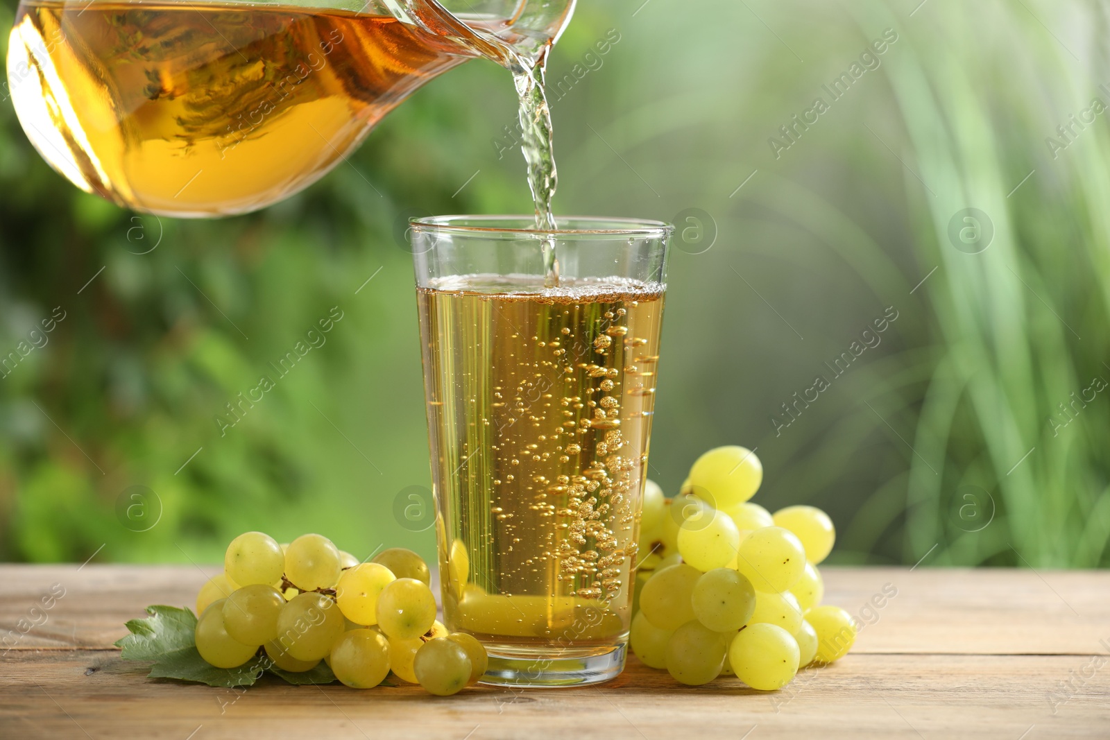 Photo of Pouring tasty grape juice into glass at wooden table outdoors, closeup