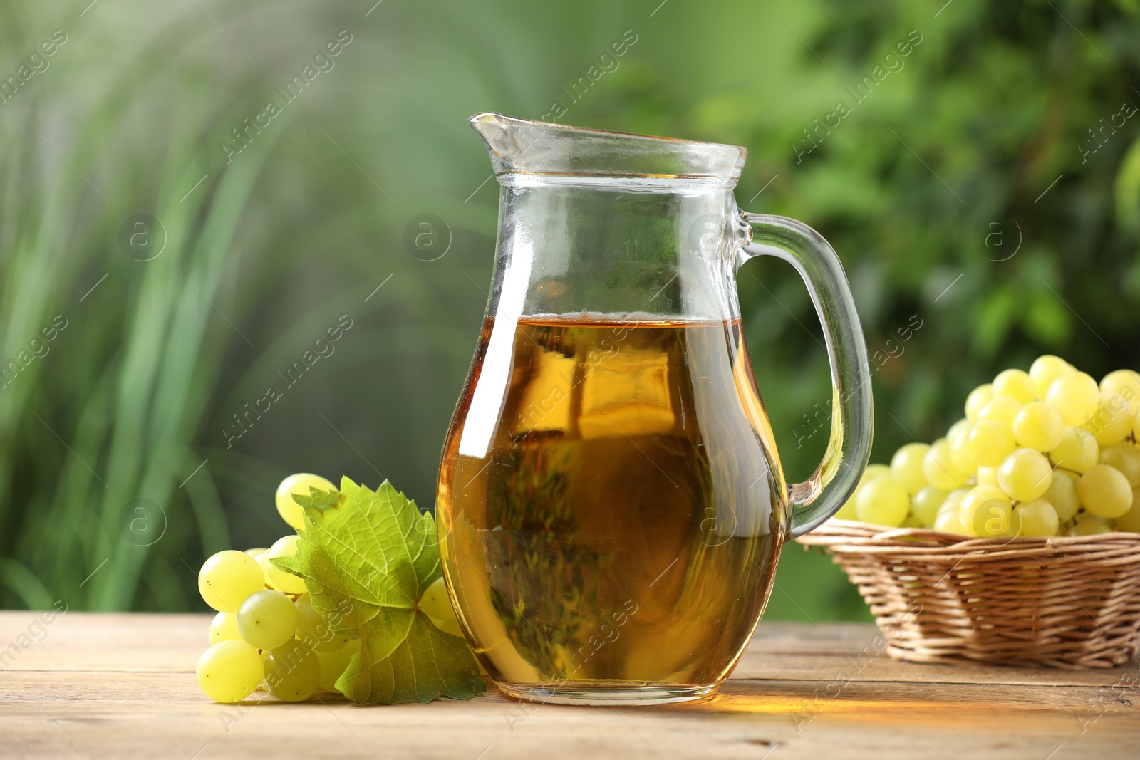 Photo of Tasty juice in glass jug, grapes and leaf on wooden table outdoors