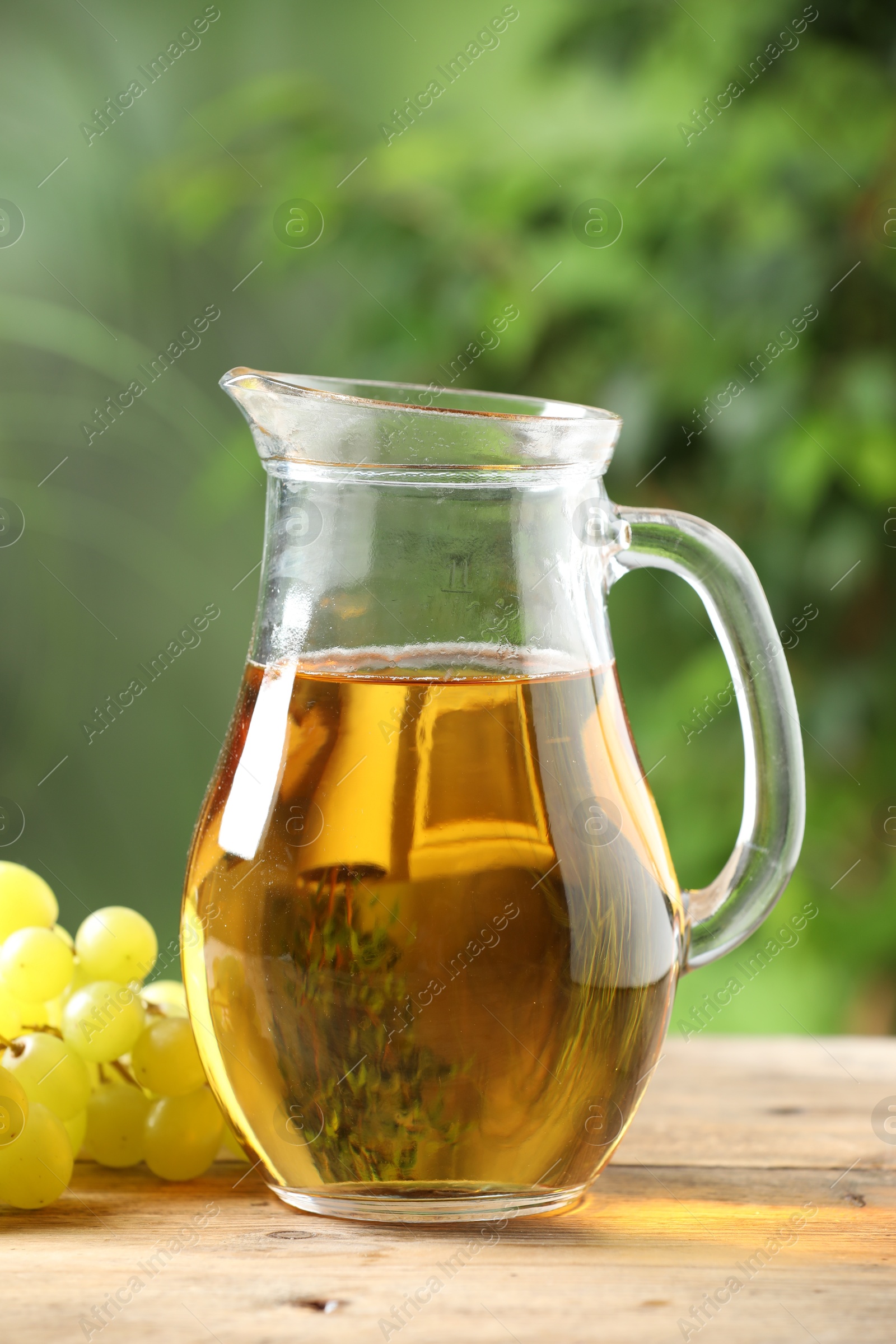 Photo of Tasty juice in glass jug and grapes on wooden table outdoors