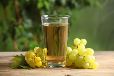 Tasty juice in glass, grapes and leaf on wooden table, closeup