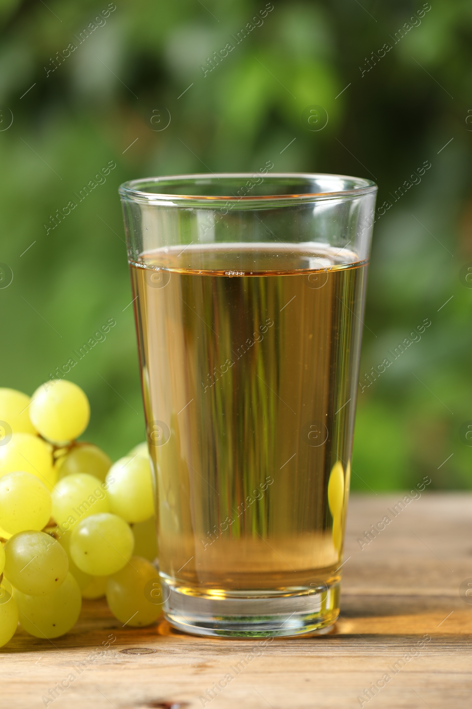 Photo of Tasty juice in glass and grapes on wooden table, closeup