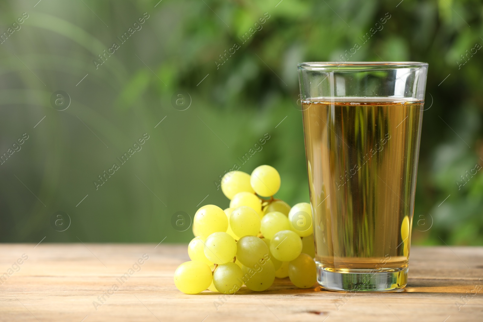 Photo of Tasty juice in glass and grapes on wooden table, space for text