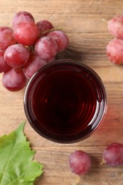 Photo of Tasty juice in glass, fresh grapes and leaf on wooden table, top view