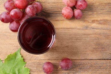 Tasty juice in glass, fresh grapes and leaf on wooden table, top view. Space for text