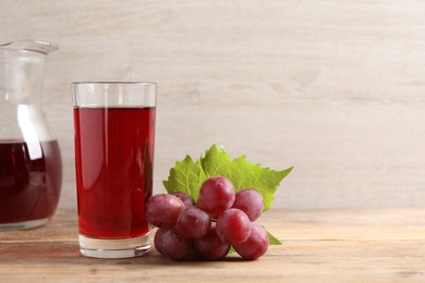 Photo of Tasty juice in glass, fresh grapes and leaf on wooden table, space for text