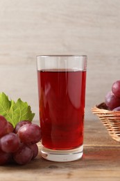 Photo of Tasty juice in glass, fresh grapes and leaf on wooden table