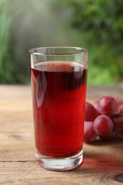 Photo of Tasty juice in glass and grapes on wooden table