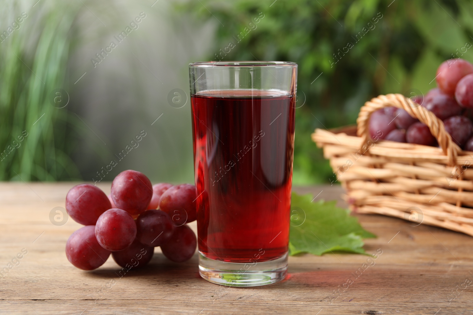 Photo of Tasty juice in glass, fresh grapes and leaf on wooden table