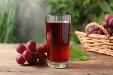 Photo of Tasty juice in glass, fresh grapes and leaf on wooden table