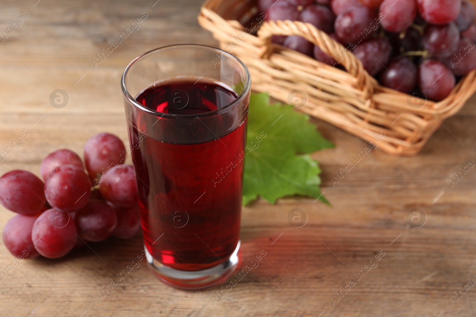 Photo of Tasty juice in glass, fresh grapes and leaf on wooden table, closeup