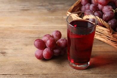 Photo of Tasty juice in glass and grapes on wooden table, closeup. Space for text