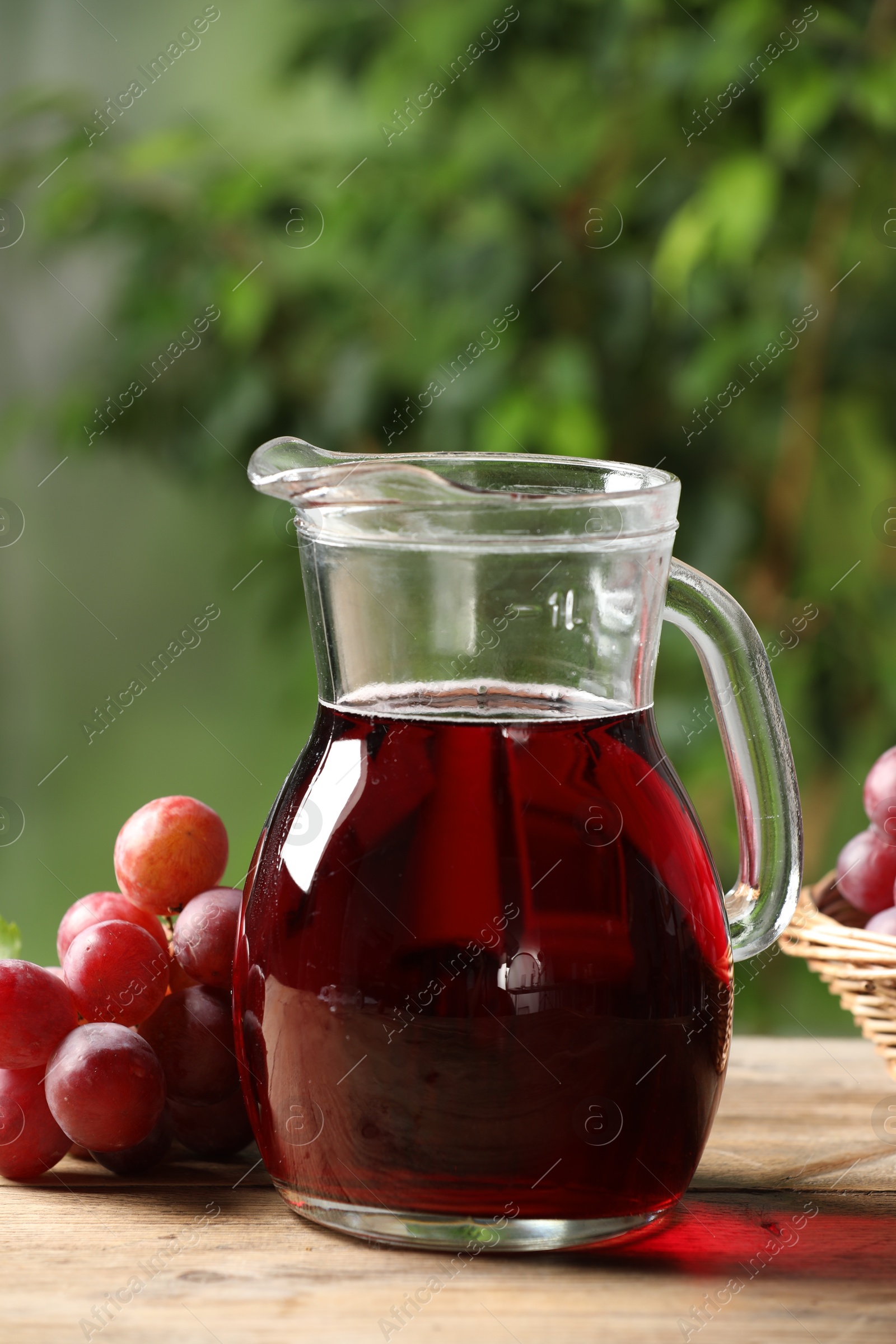 Photo of Tasty juice in glass jug and grapes on wooden table outdoors