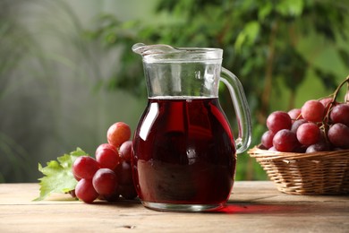 Photo of Tasty juice in glass jug and grapes on wooden table outdoors