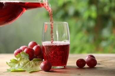 Pouring tasty grape juice into glass at wooden table outdoors, closeup