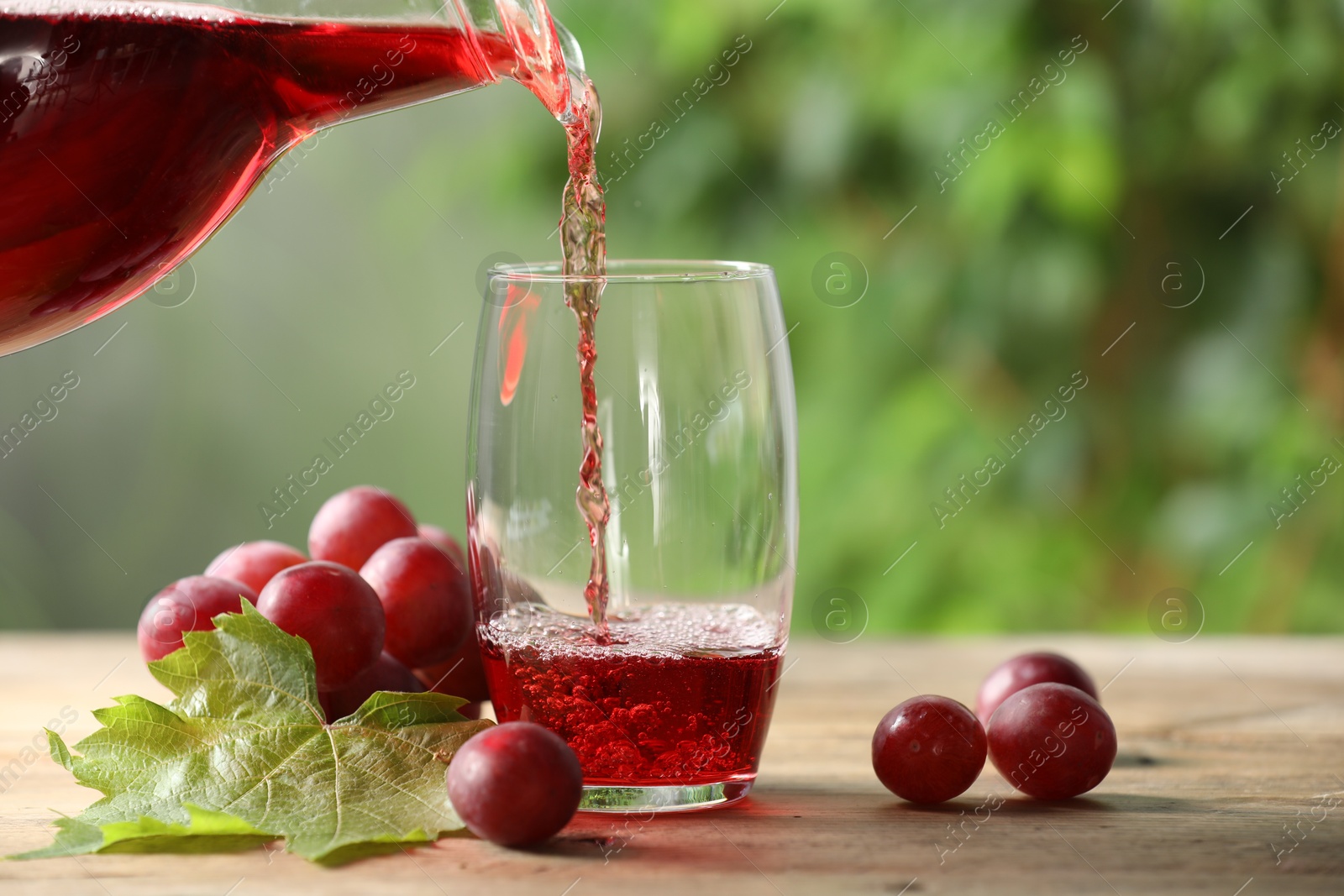 Photo of Pouring tasty grape juice into glass at wooden table outdoors, closeup