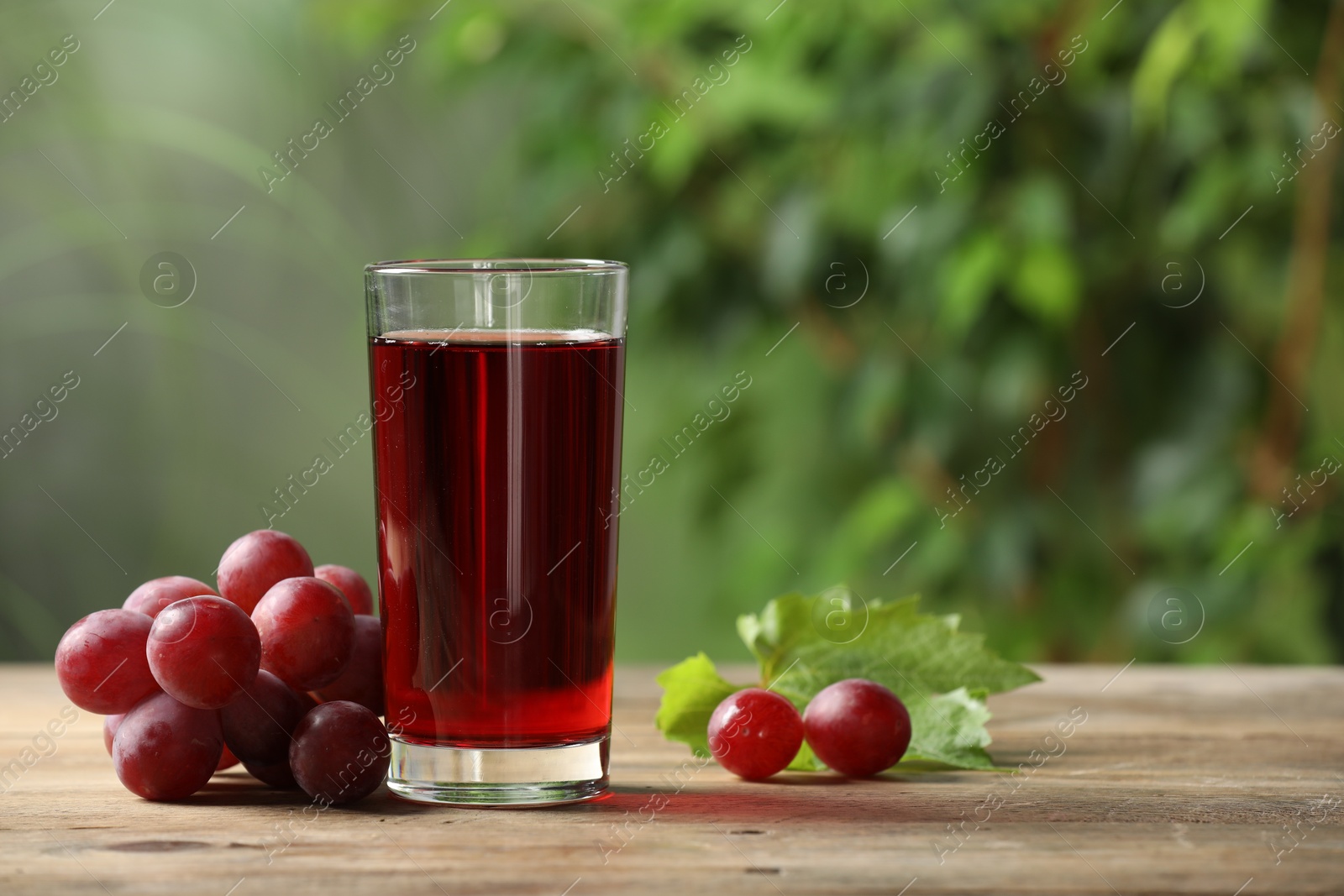 Photo of Tasty juice in glass, fresh grapes and leaf on wooden table. Space for text