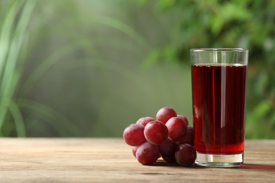 Photo of Tasty juice in glass and fresh grapes on wooden table, space for text