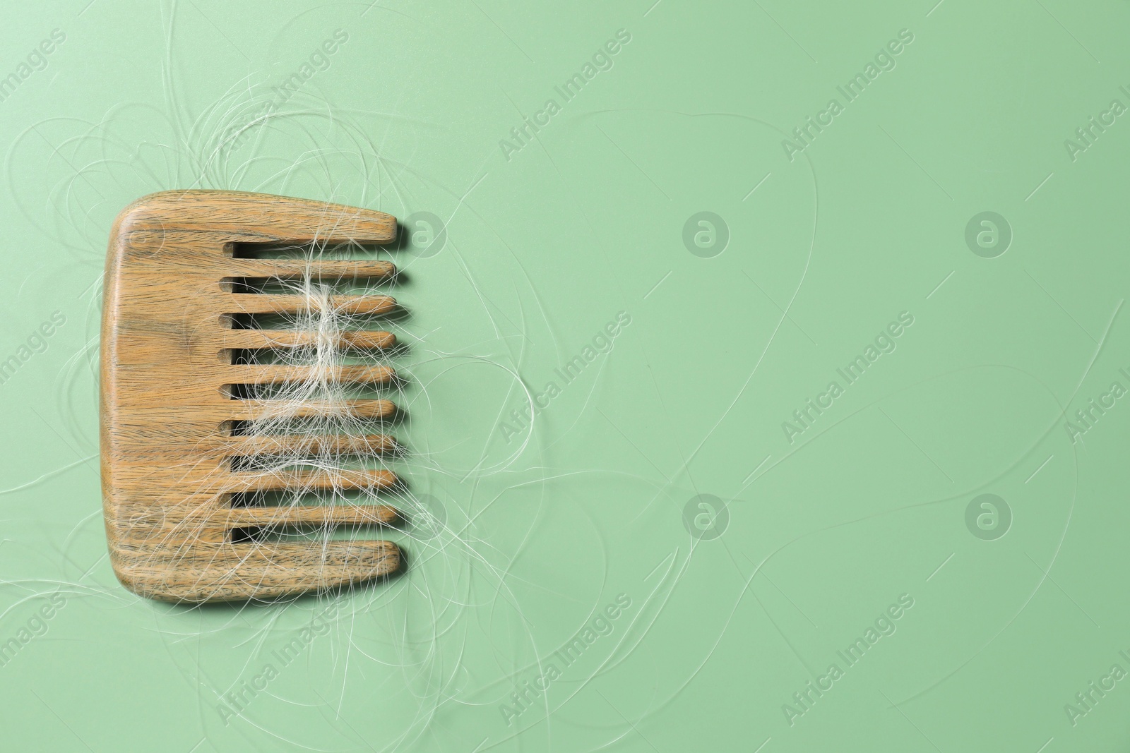 Photo of Comb with lost hair on green background, top view. Space for text