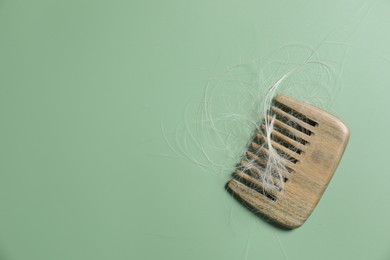 Photo of Comb with lost hair on green background, top view. Space for text