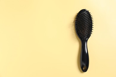 Photo of Brush with lost hair on yellow background, top view. Space for text