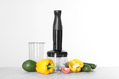 Hand blender kit and fresh vegetables on gray table against white background