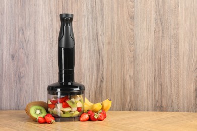 Photo of Hand blender kit, fresh fruits and strawberries on wooden table, space for text