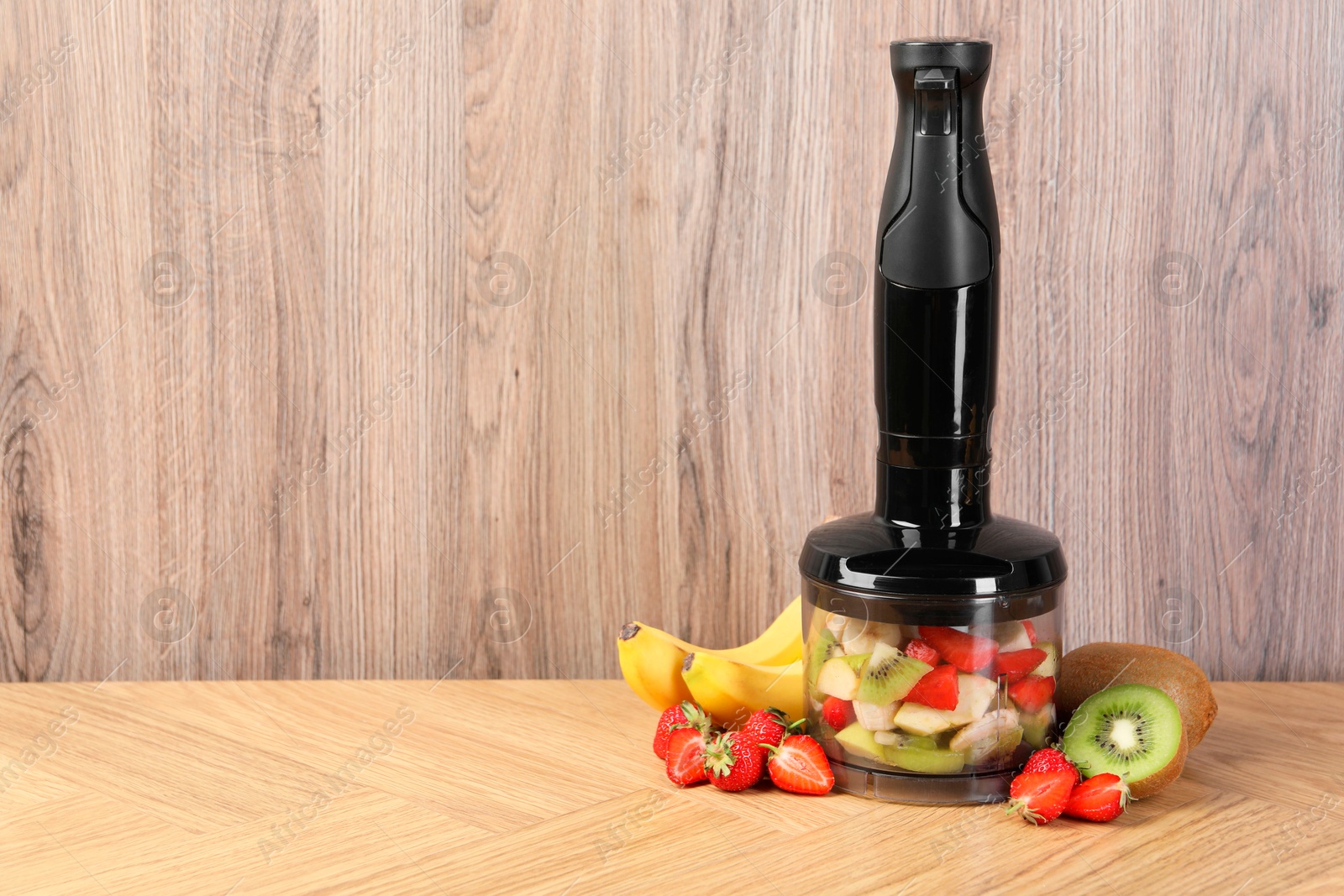 Photo of Hand blender kit, fresh fruits and strawberries on wooden table, space for text