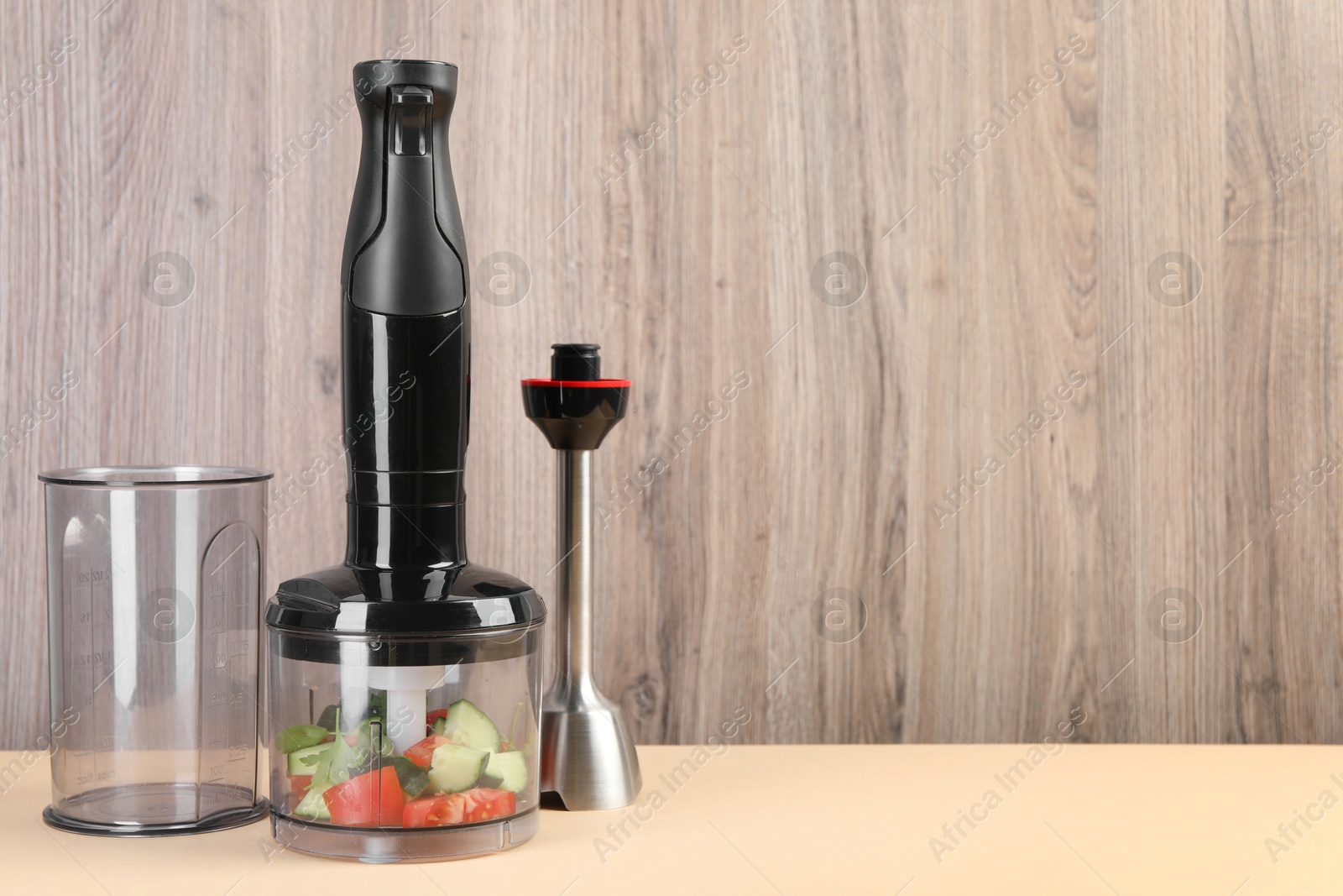 Photo of Hand blender kit with fresh vegetables and parsley on beige table against wooden background, space for text