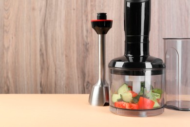 Hand blender kit with fresh vegetables and parsley on beige table against wooden background, space for text