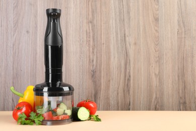 Hand blender kit, fresh vegetables and parsley on beige table against wooden background, space for text