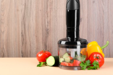 Hand blender kit, fresh vegetables and parsley on beige table against wooden background, space for text