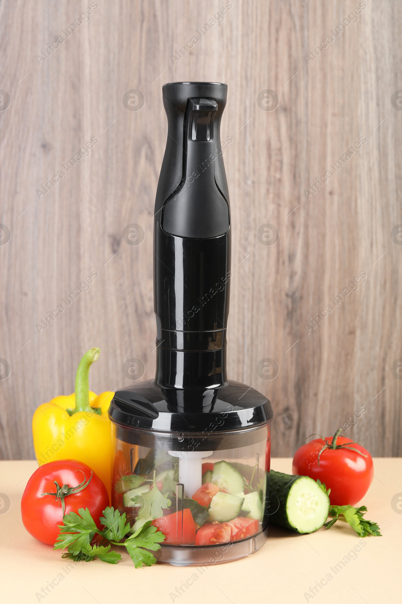 Photo of Hand blender kit, fresh vegetables and parsley on beige table against wooden background