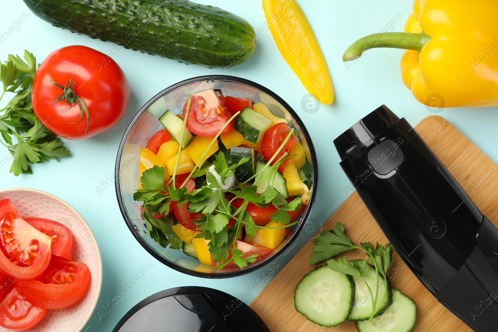 Photo of Hand blender kit, fresh vegetables and parsley on light blue background, flat lay