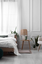 Stylish living room interior with bed, bedside table, lamp and houseplants