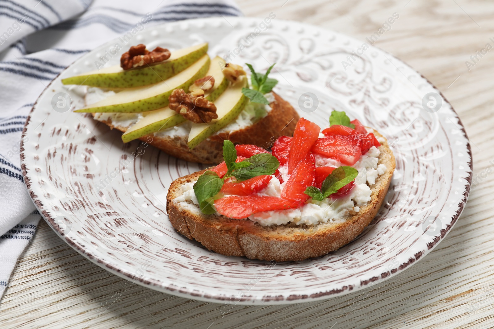 Photo of Delicious bruschettas with fresh ricotta (cream cheese), strawberry, mint and pear on wooden table