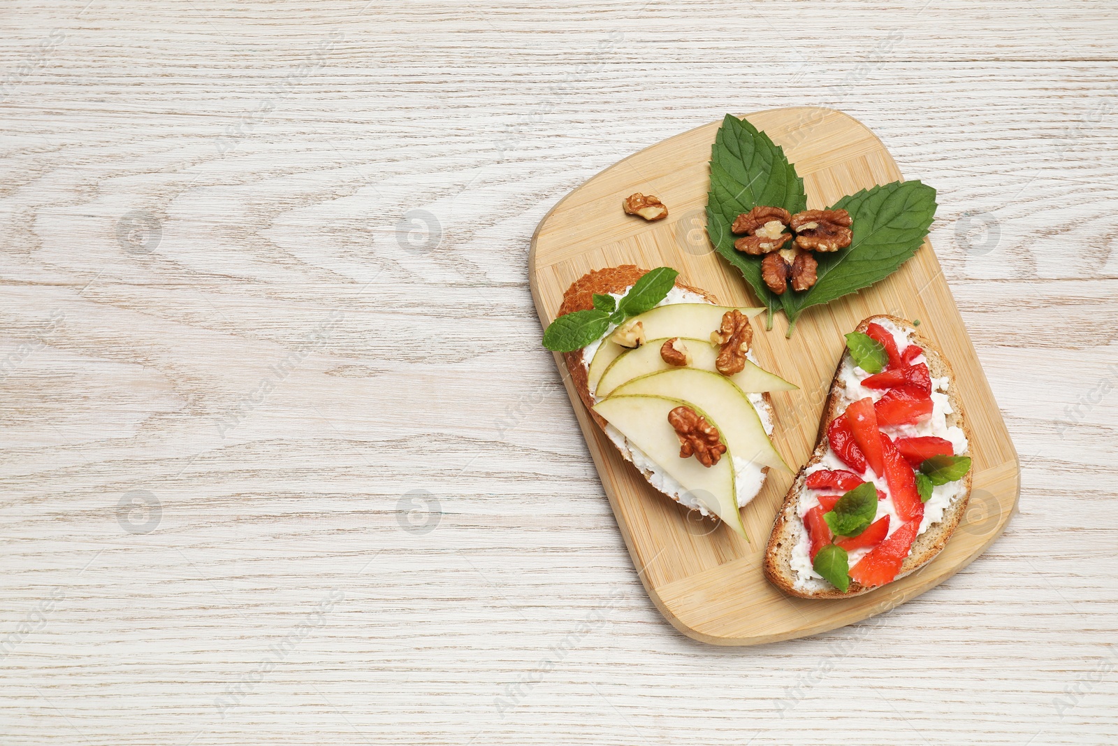 Photo of Delicious bruschettas with fresh ricotta (cream cheese), strawberry, mint and pear on wooden table, top view. Space for text