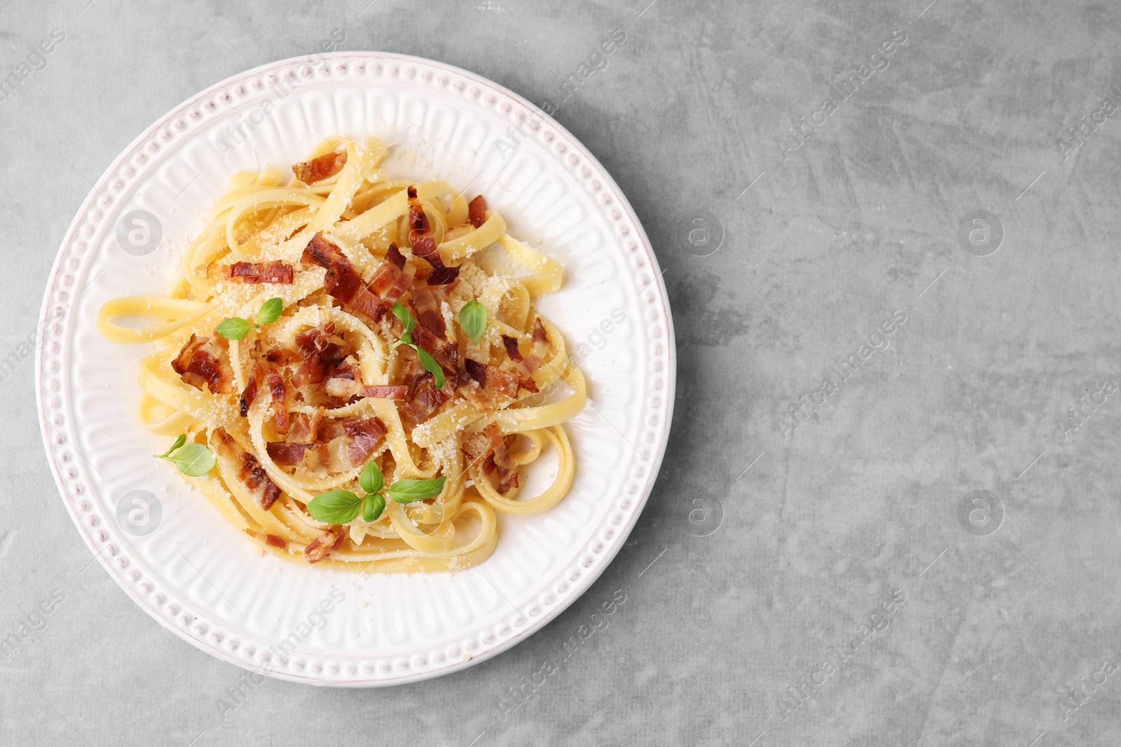 Photo of Tasty pasta with bacon and basil on light grey table, top view. Space for text