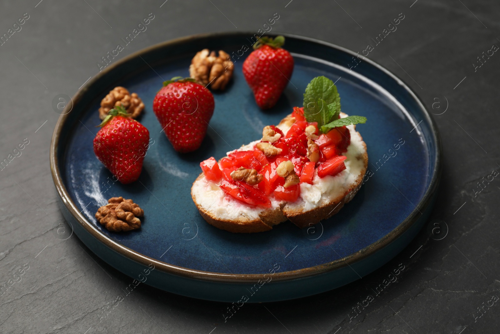 Photo of Delicious ricotta bruschetta with strawberry and mint on black table