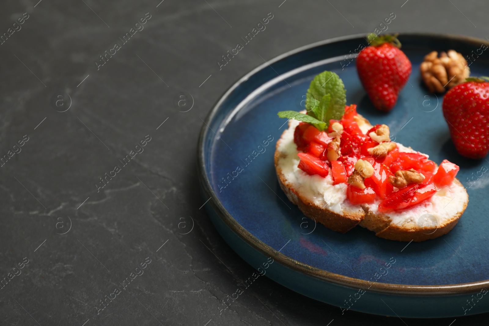 Photo of Delicious ricotta bruschetta with strawberry and mint on black table. Space for text