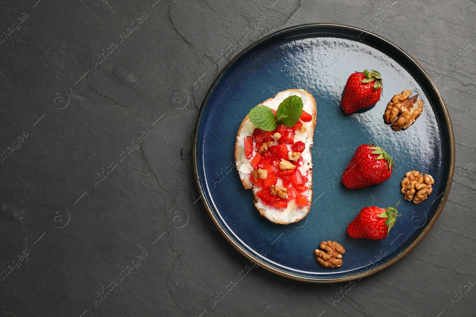 Photo of Delicious ricotta bruschetta with strawberry and mint on black table, top view. Space for text