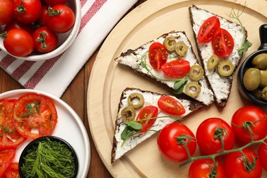 Photo of Delicious ricotta bruschettas with fresh tomatoes, olives and greens on wooden table, flat lay