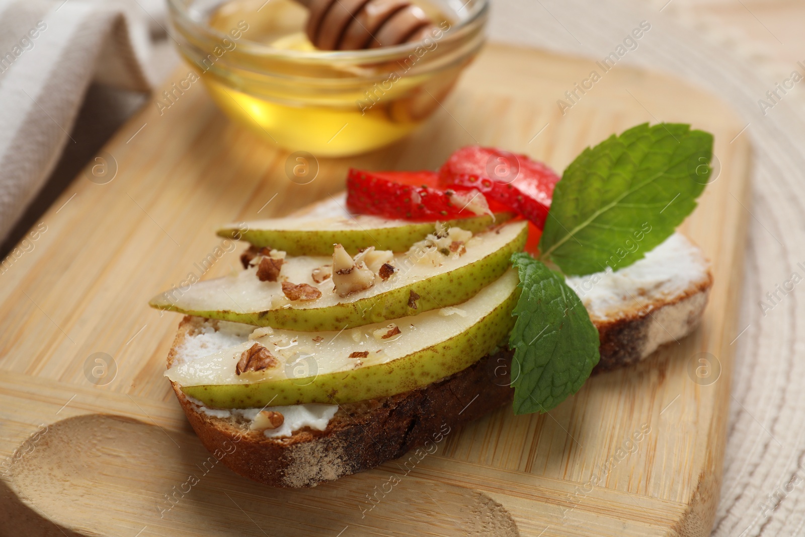 Photo of Delicious ricotta bruschetta with pear, strawberry and walnut on wooden table, closeup